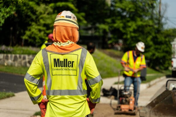 A muller crew member standing on the side of a jobsite watching other members working in the background.
