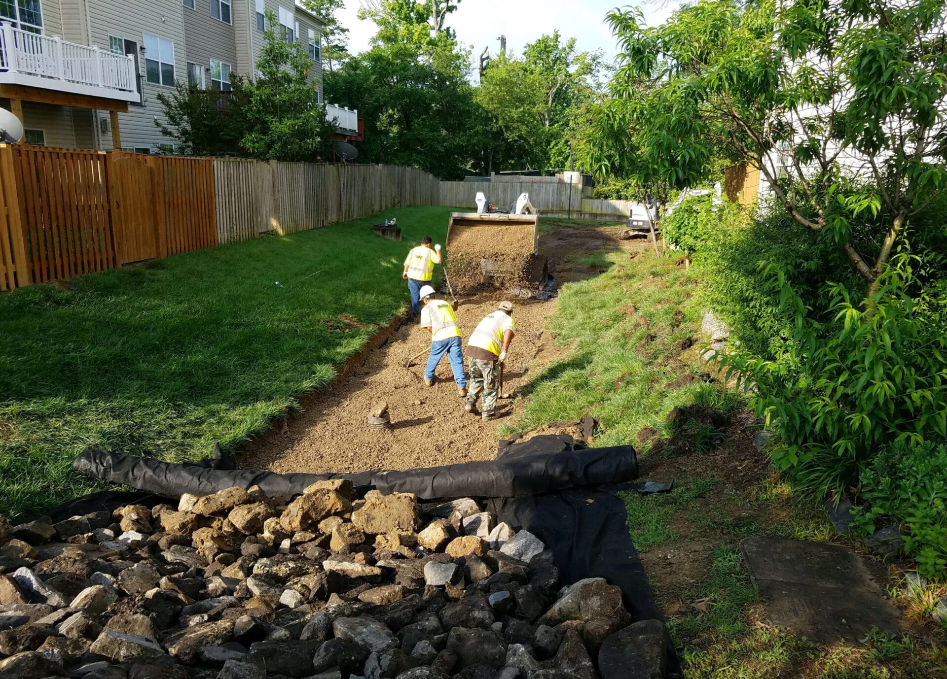 Muller crew members working to dig up dirt and lay down fabric with stones on it in the alley of a suburban neighborhood.