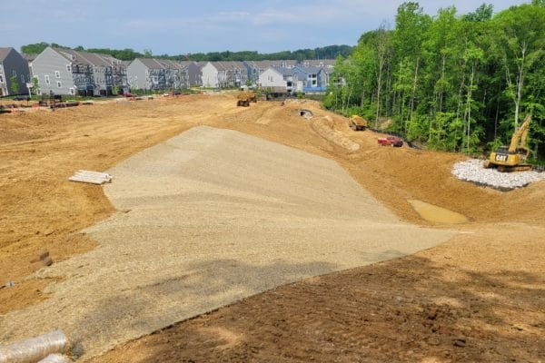 Dirt and erosion control blanket on the edge of a hill leading toward the woods on the outside perimeter of a suburban neighborhood.