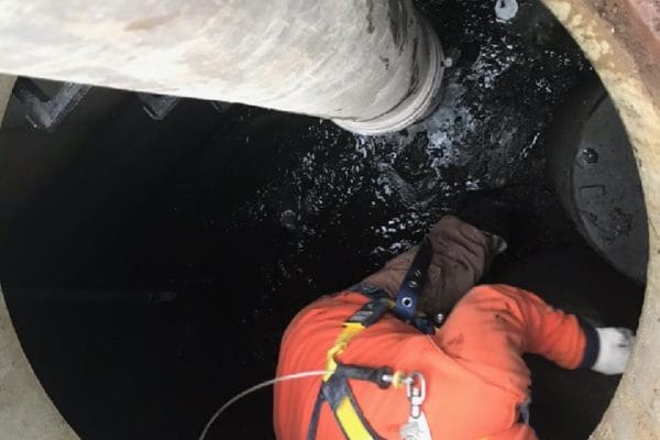 A worker inside a stormwater valult with a large pipe inside to help maintain and clean it.