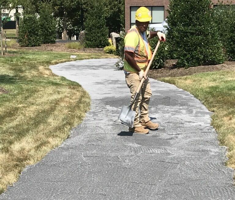 Muller worker with shovel in hand on an asphalt path.